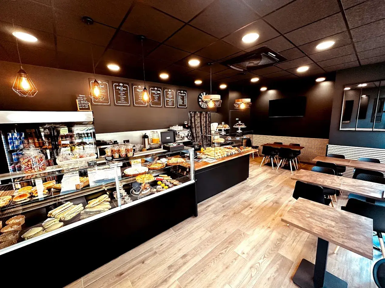 L'intérieur du café : tables en bois, chaises noires, suspensions et comptoir de pâtisseries